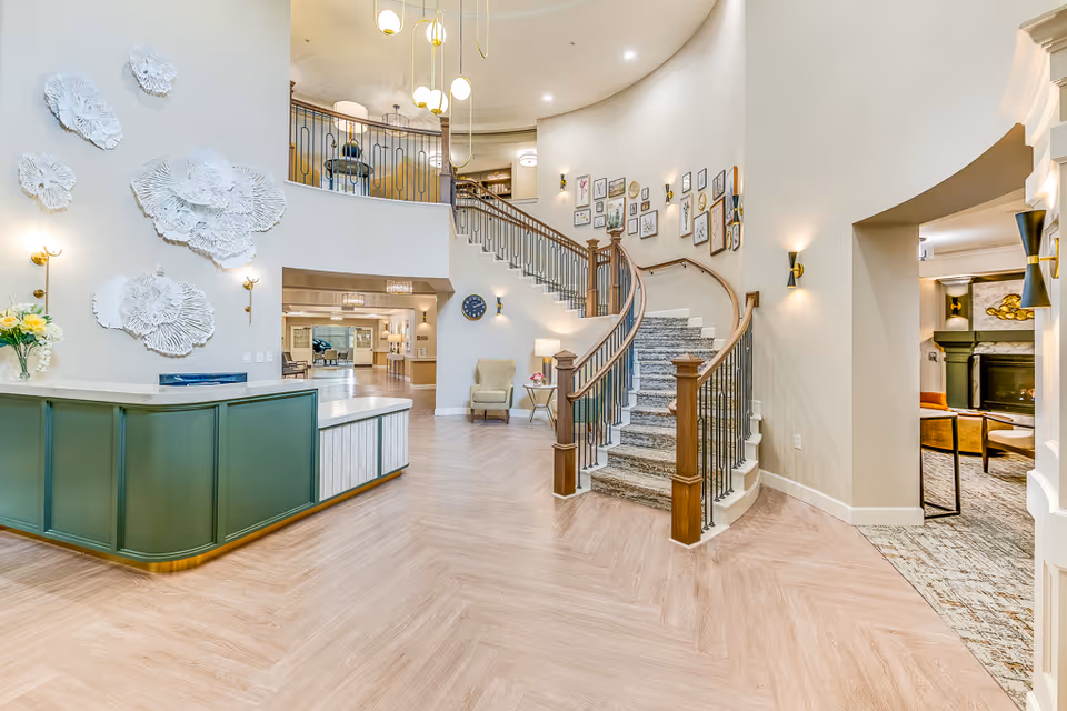 Spacious, elegant lobby with a curved staircase, green reception desk, wall art, and seating areas.