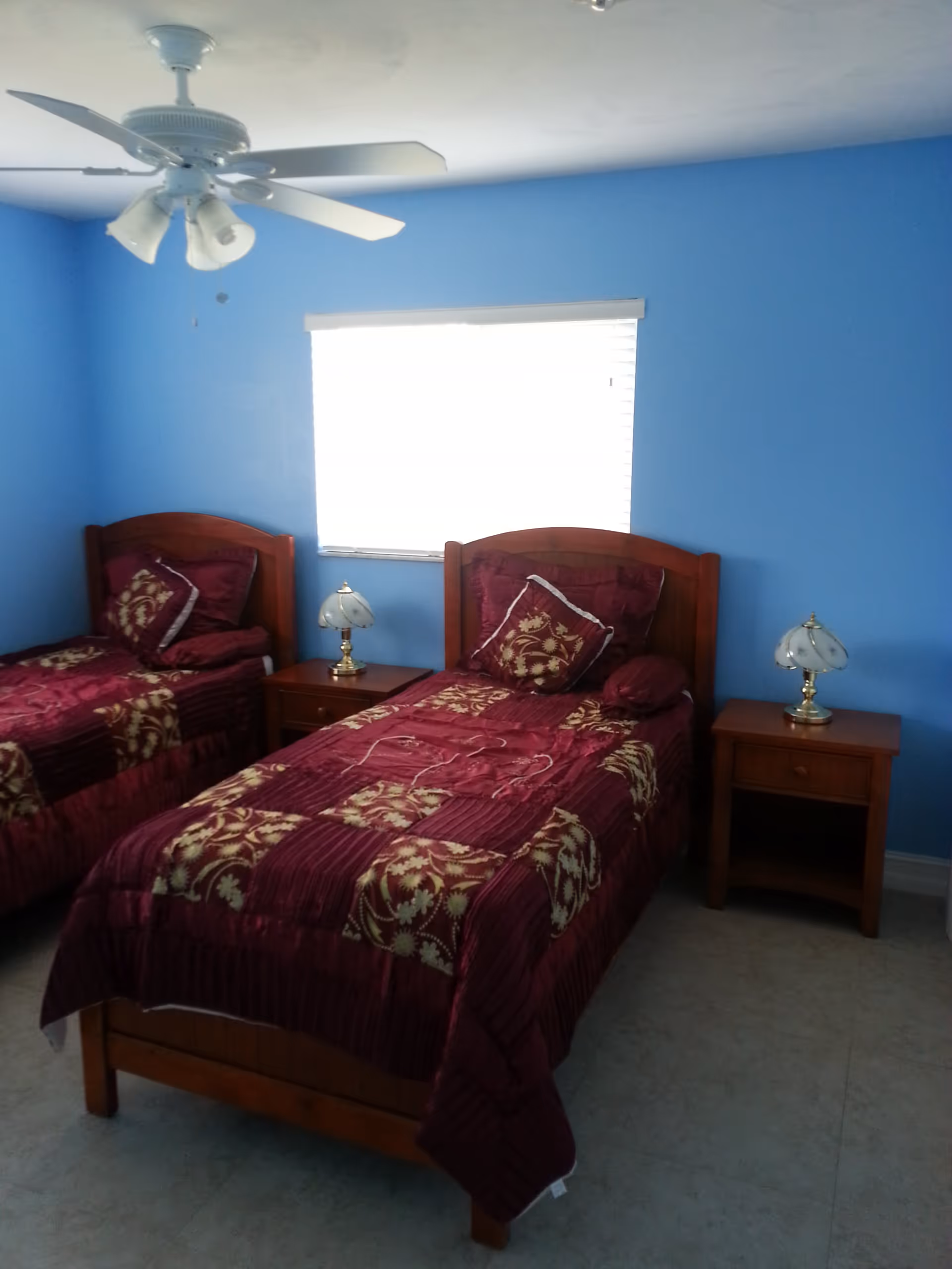 Two twin beds with maroon patterned bedspreads, wooden headboards, and nightstands with lamps in a blue-walled bedroom.
