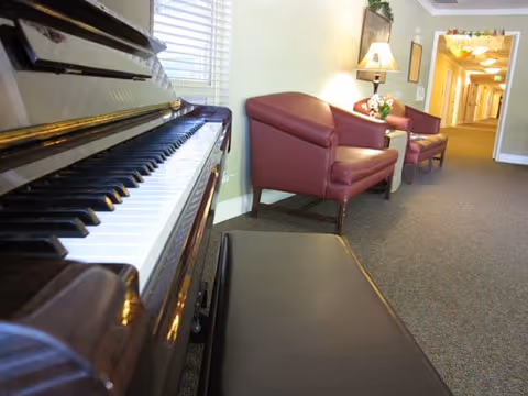 Hallway seating area with a piano in the foreground and two red armchairs with a lamp further down the corridor.