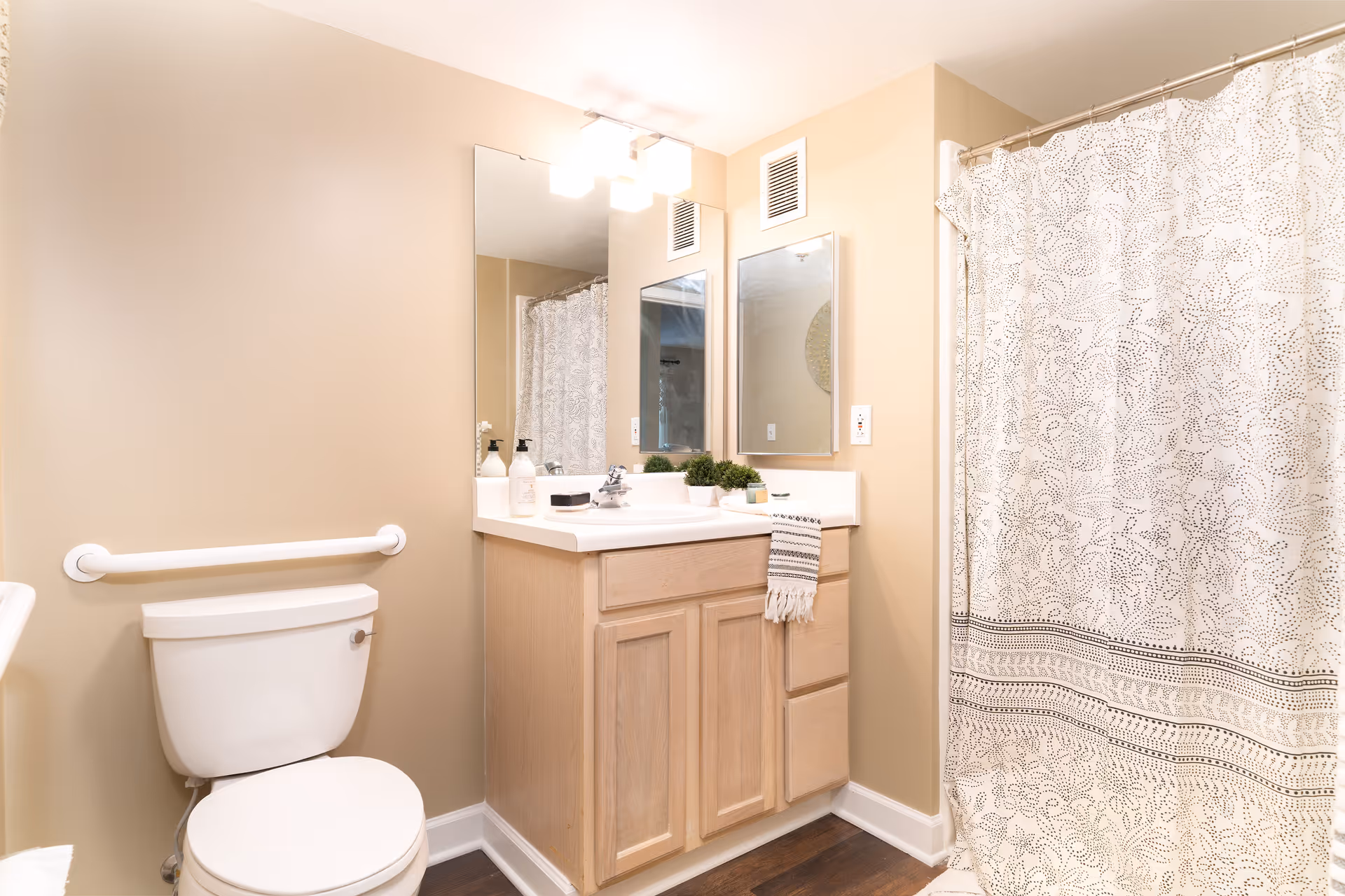 Well-lit bathroom with a toilet, wooden vanity and mirror, sink accessories, and a patterned shower curtain.