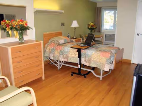 Two hospital beds in a furnished patient room with dresser, lamp, and laptop.