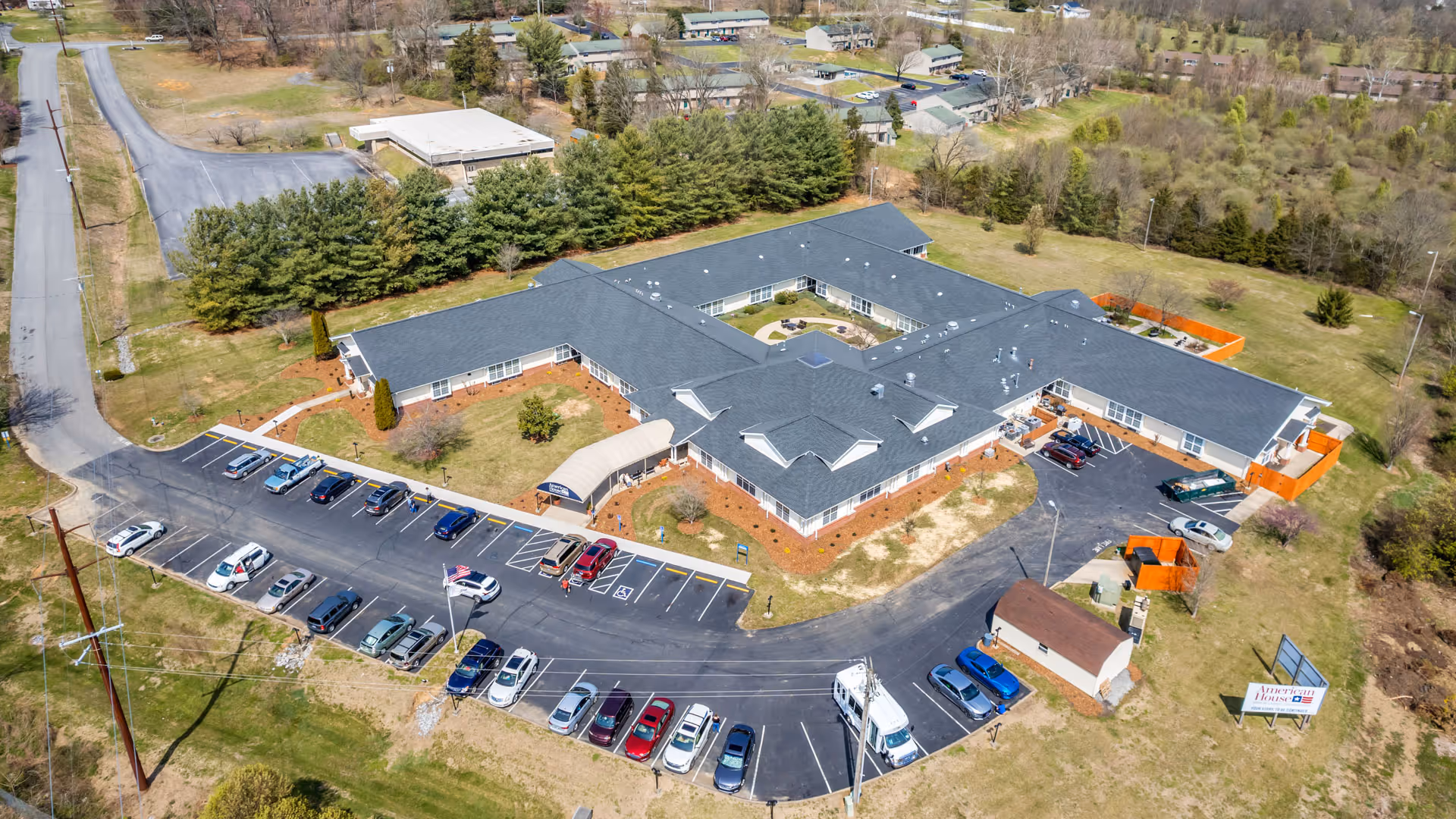 Aerial view of a single-story U-shaped senior living facility with a parking lot, surrounding lawns, and nearby roads.