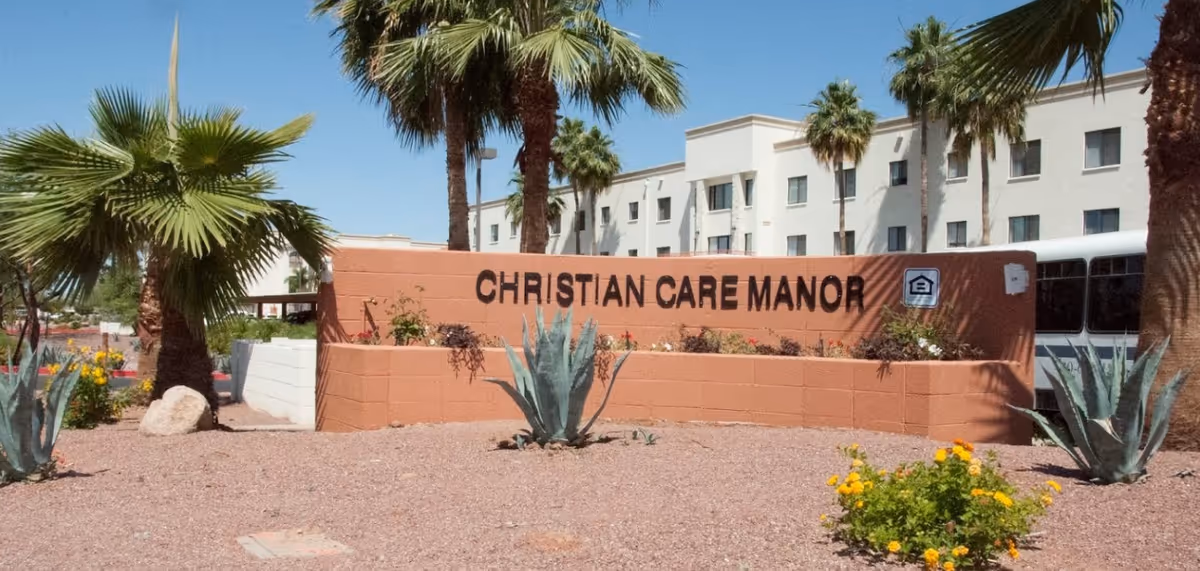 Entrance sign reading "Christian Care Manor" in front of a multi-story building with palm trees and desert landscaping.