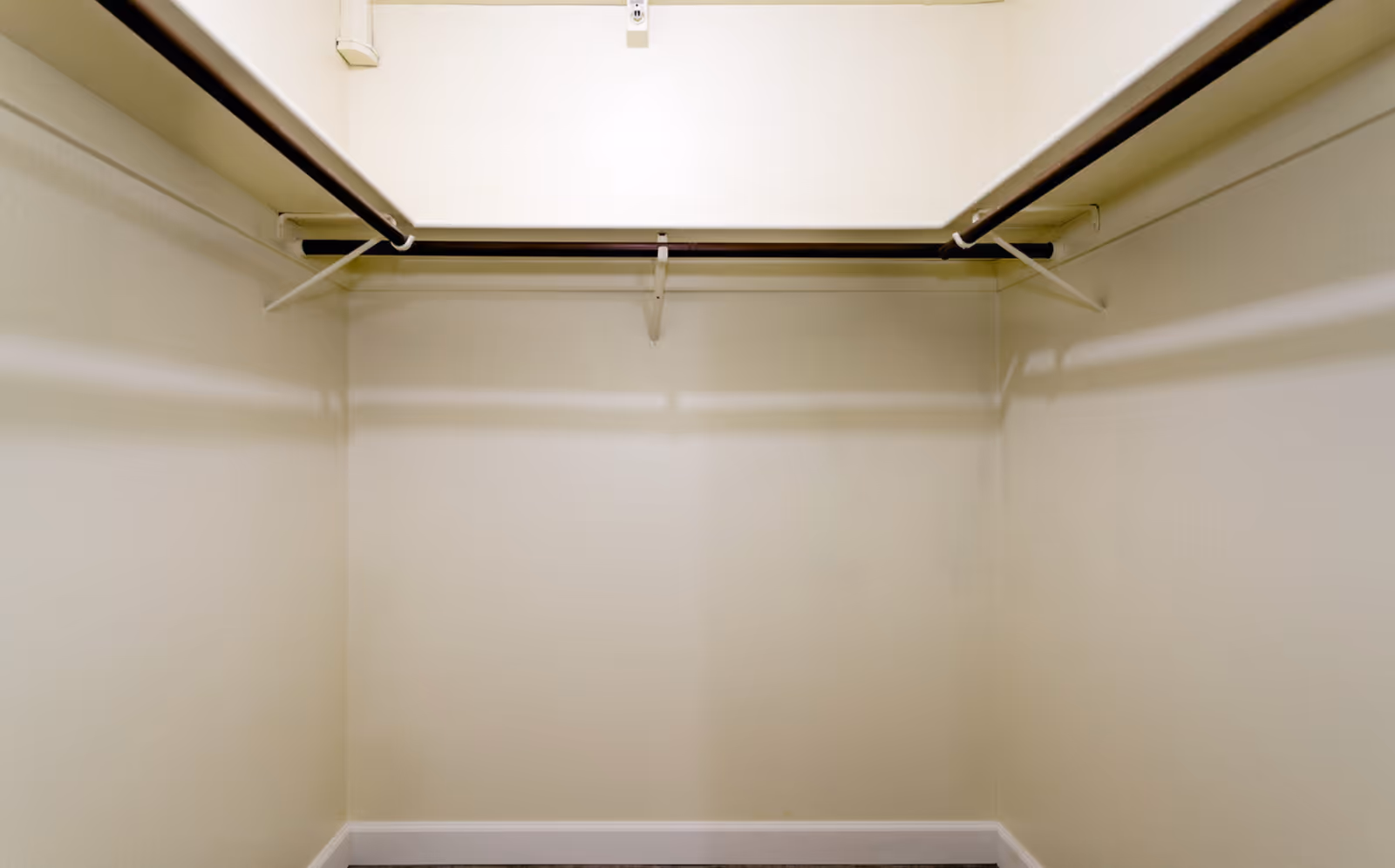 Empty walk-in closet with beige walls, a shelf and hanging rods.