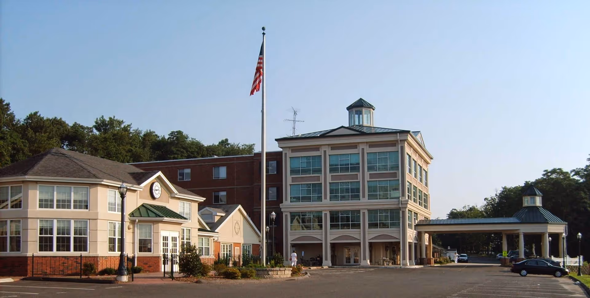 Front exterior of a multi-story nursing and rehabilitation center with a flagpole, parking area, and covered entrance.