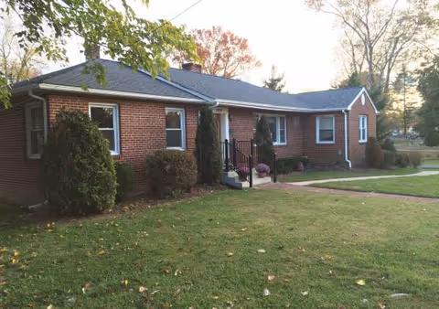 Brick, single-story assisted living facility front with lawn, shrubs, and a walkway.