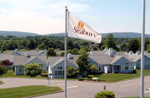 Flag with Seabury logo in foreground; row of light blue buildings on a campus.