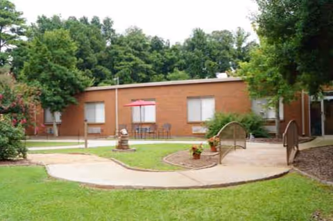 Brick single-story facility with outdoor courtyard, curved path, small bridge, and chairs.