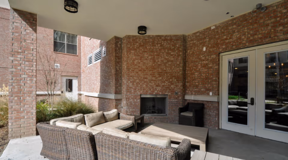 Covered outdoor patio with wicker sectional seating, a coffee table, and a brick fireplace under a building overhang.