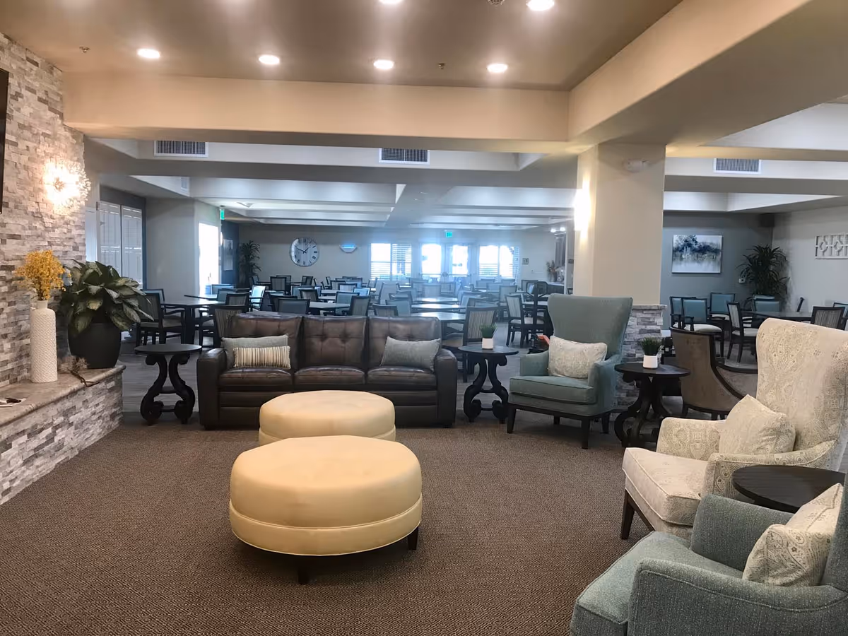 Spacious senior living common area with sofas, armchairs, round ottomans and dining tables visible in the background.