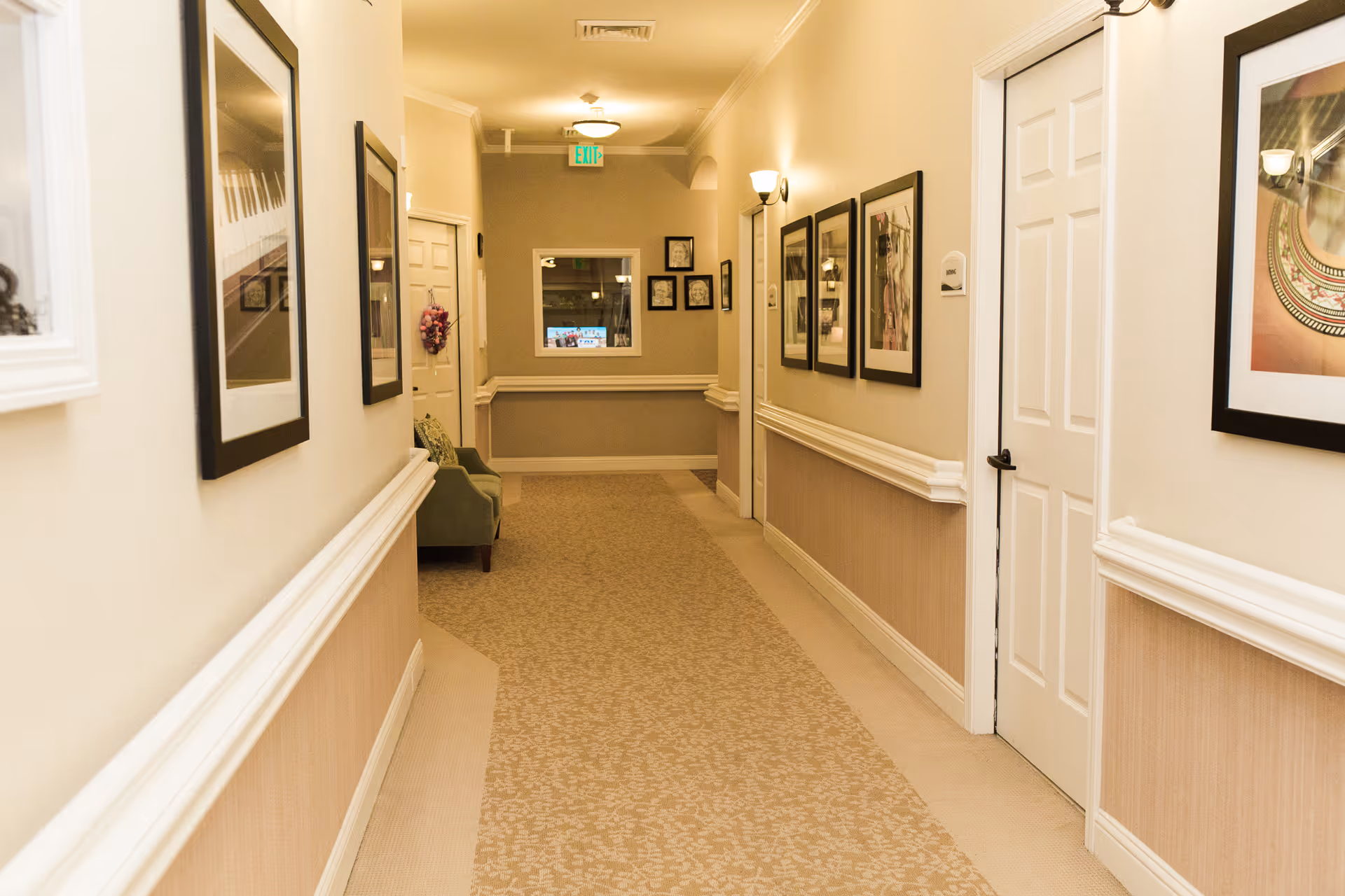 Well-lit carpeted interior hallway with framed artwork, doors, and seating.