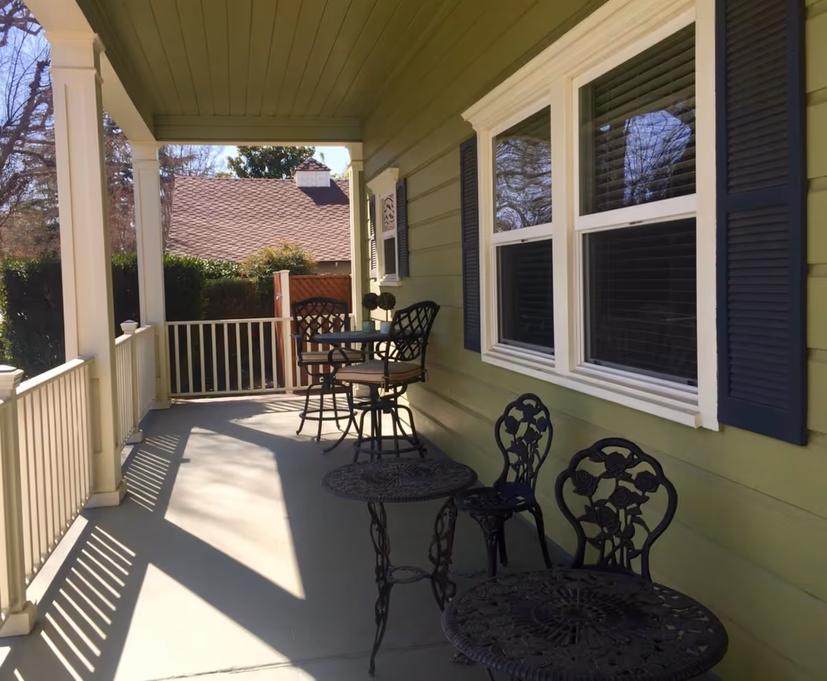 Westchester Home exterior porch with green siding and black wrought-iron tables.