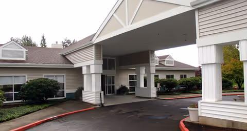 Exterior view of the entrance to Brookdale Mt. Hood senior living facility with a covered drop-off area, beige siding, and surrounding greenery.