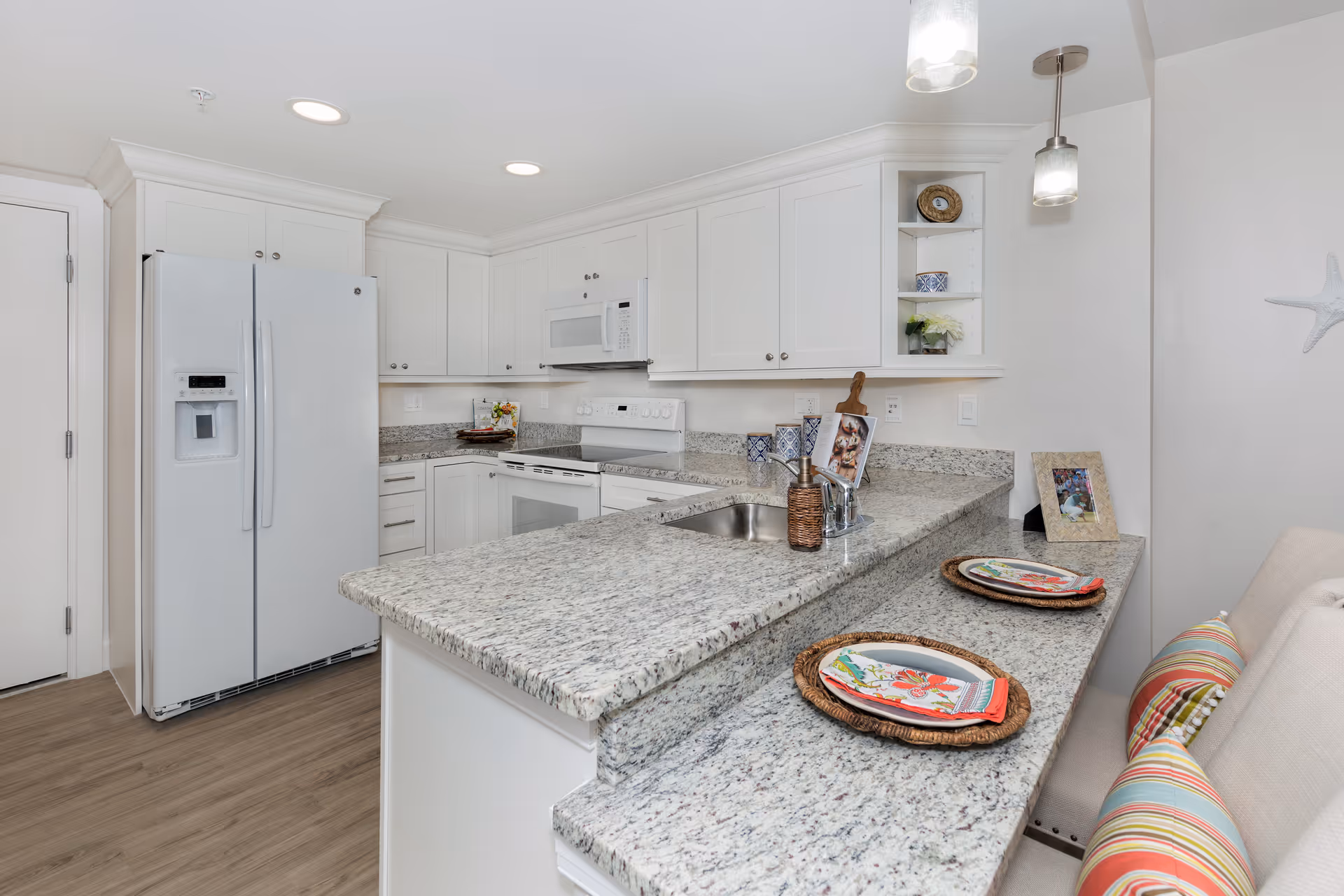 Bright modern kitchen with white cabinetry, granite countertops, a breakfast bar with place settings, and integrated appliances.