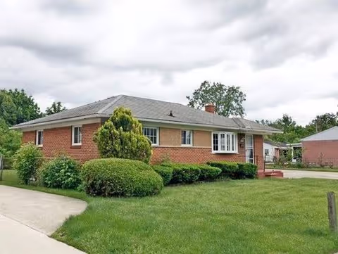 Brick, single-story senior living facility with manicured lawn and shrubs.