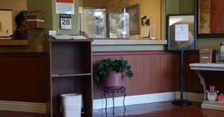 Reception area with a front desk, plant, calendar, and staff in a senior living lobby.