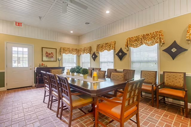 A dining room with a large wooden table surrounded by chairs, featuring decorative curtains and a warm, inviting atmosphere.