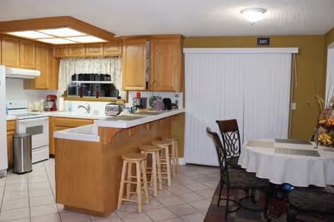 Well-lit kitchen with oak cabinets, a center island with three stools, white appliances, and an adjacent dining table.