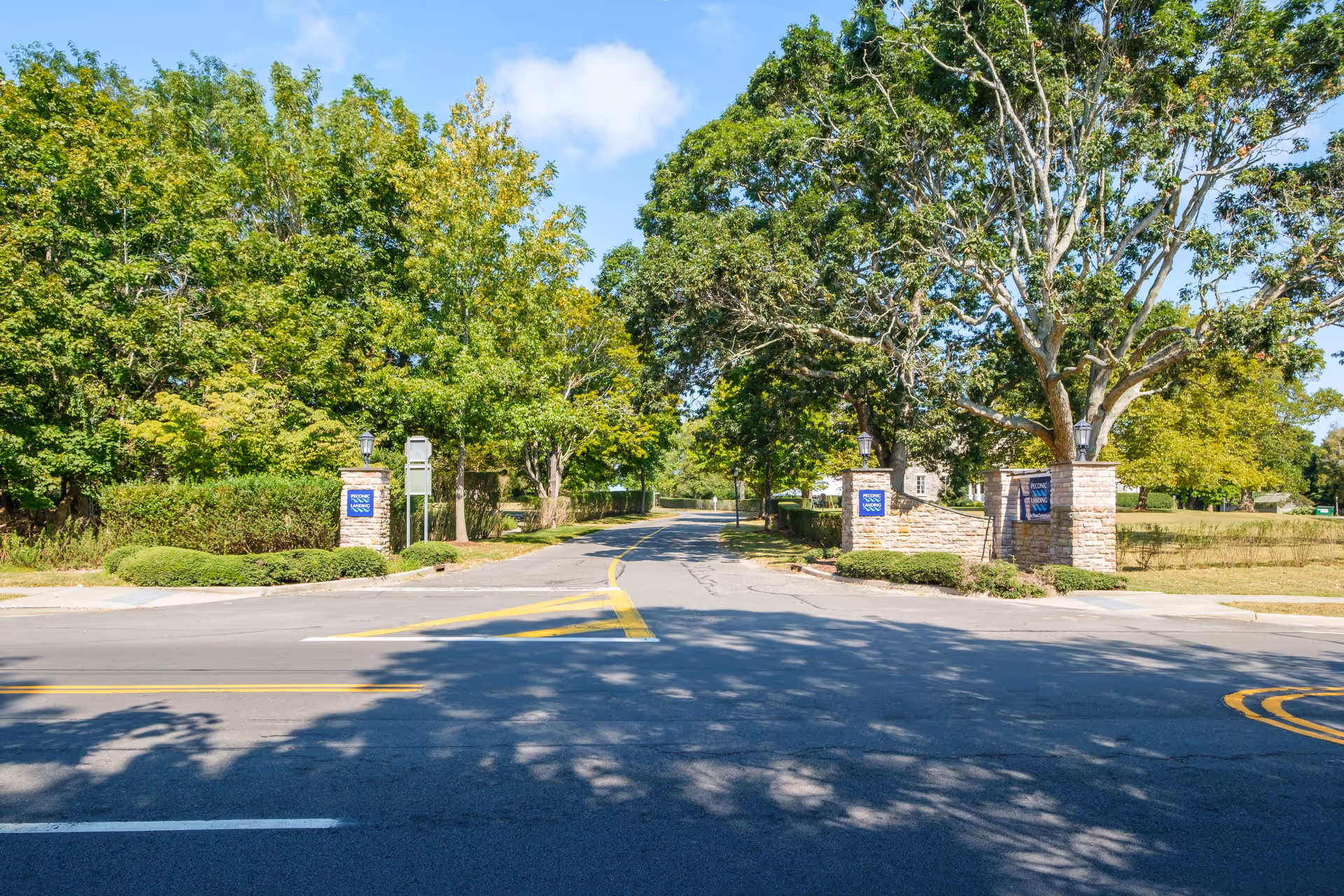 Tree-lined entrance driveway with stone pillar gateway and landscaping leading into the Peconic Landing community.
