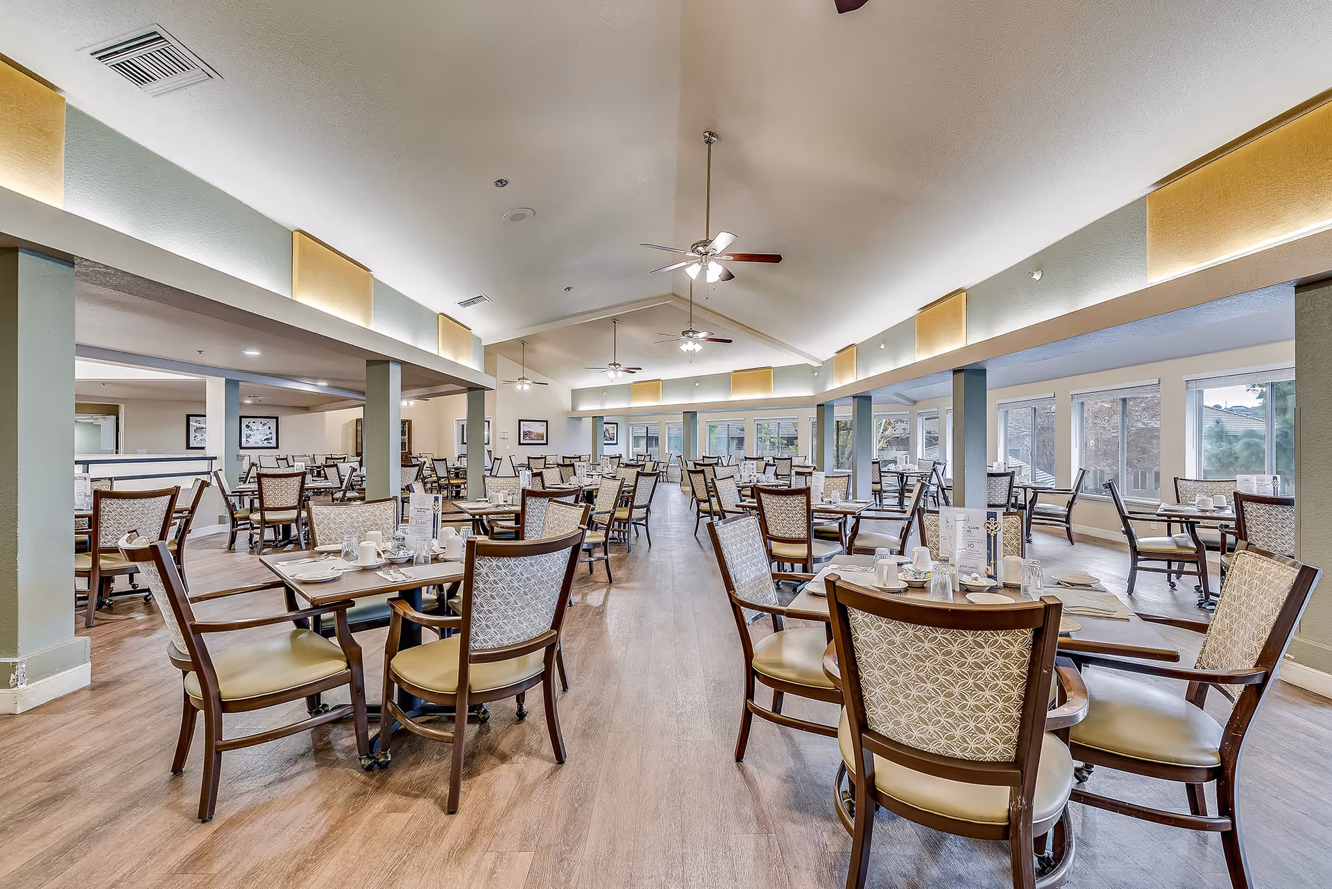 Spacious, well-lit dining room with multiple set tables and chairs in a senior living facility.