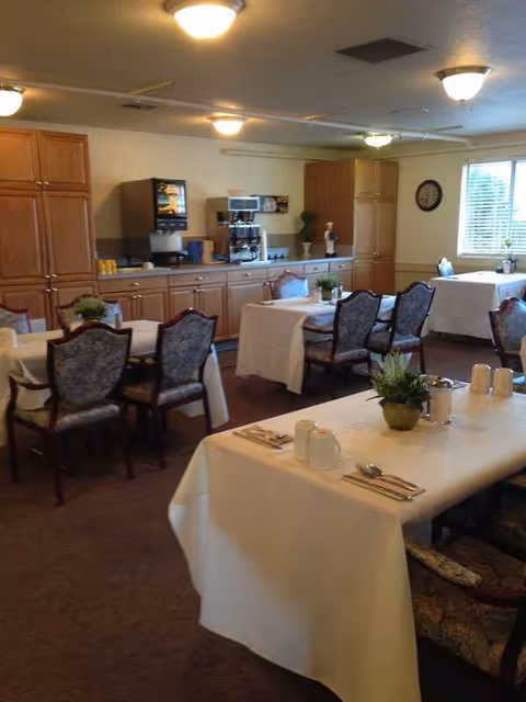 A dining room with white tablecloths, chairs, and a beverage station along wooden cabinets.