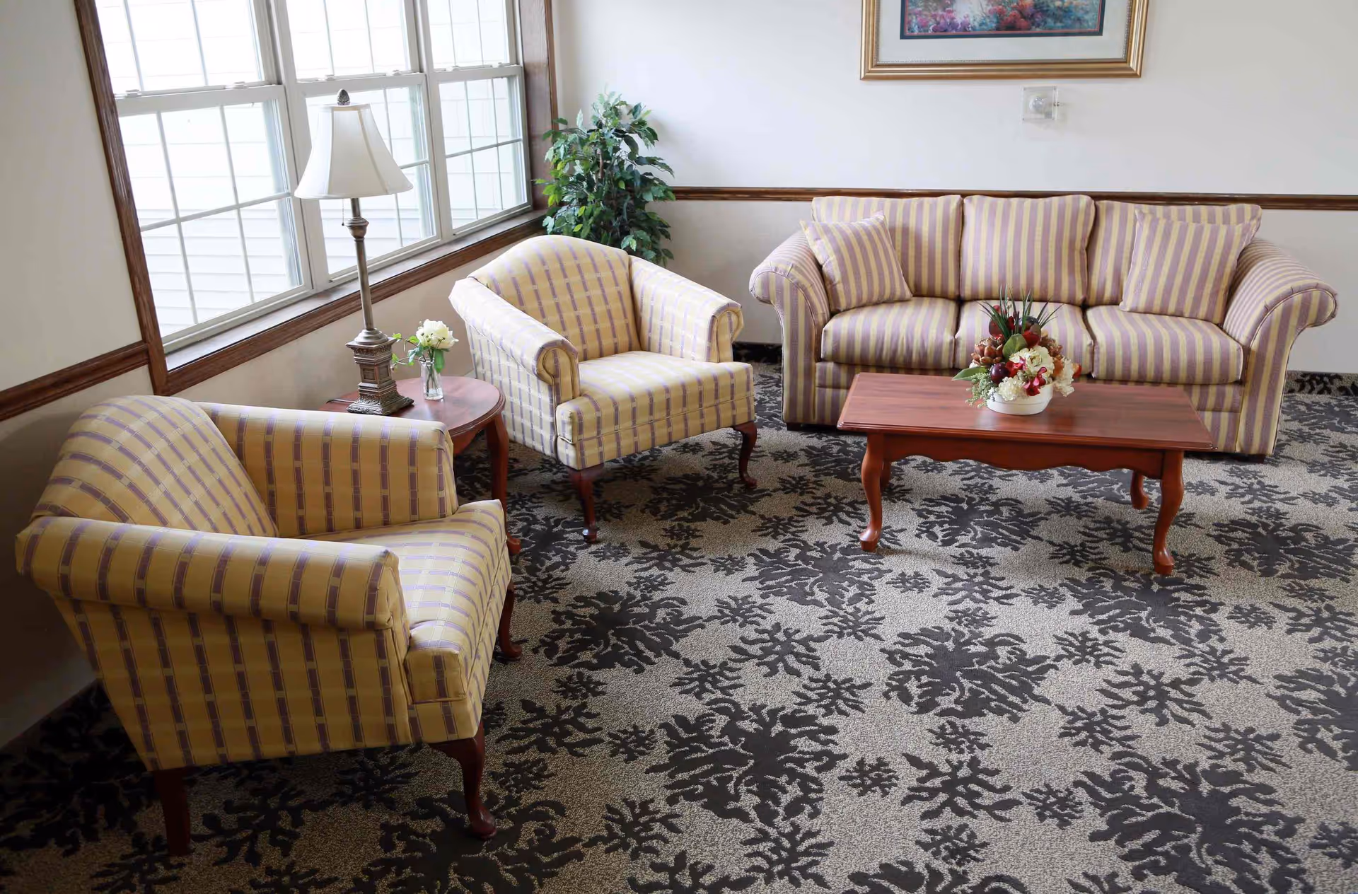 Sunlit sitting area with a striped sofa and two matching armchairs around a wooden coffee table on a patterned carpet.