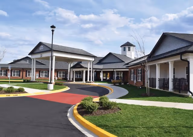 Senior living facility exterior with brick building, circular driveway, and covered entrance.