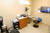 Small salon-like room with two styling chairs, a counter and sink with hair-care supplies, and a wall-mounted TV.