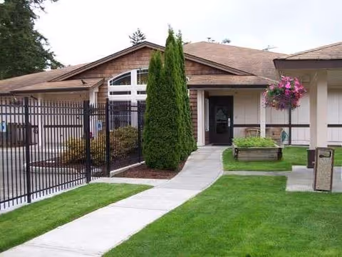 Exterior view of Pioneer Place senior living facility with walkway, greenery, bench, and fencing.