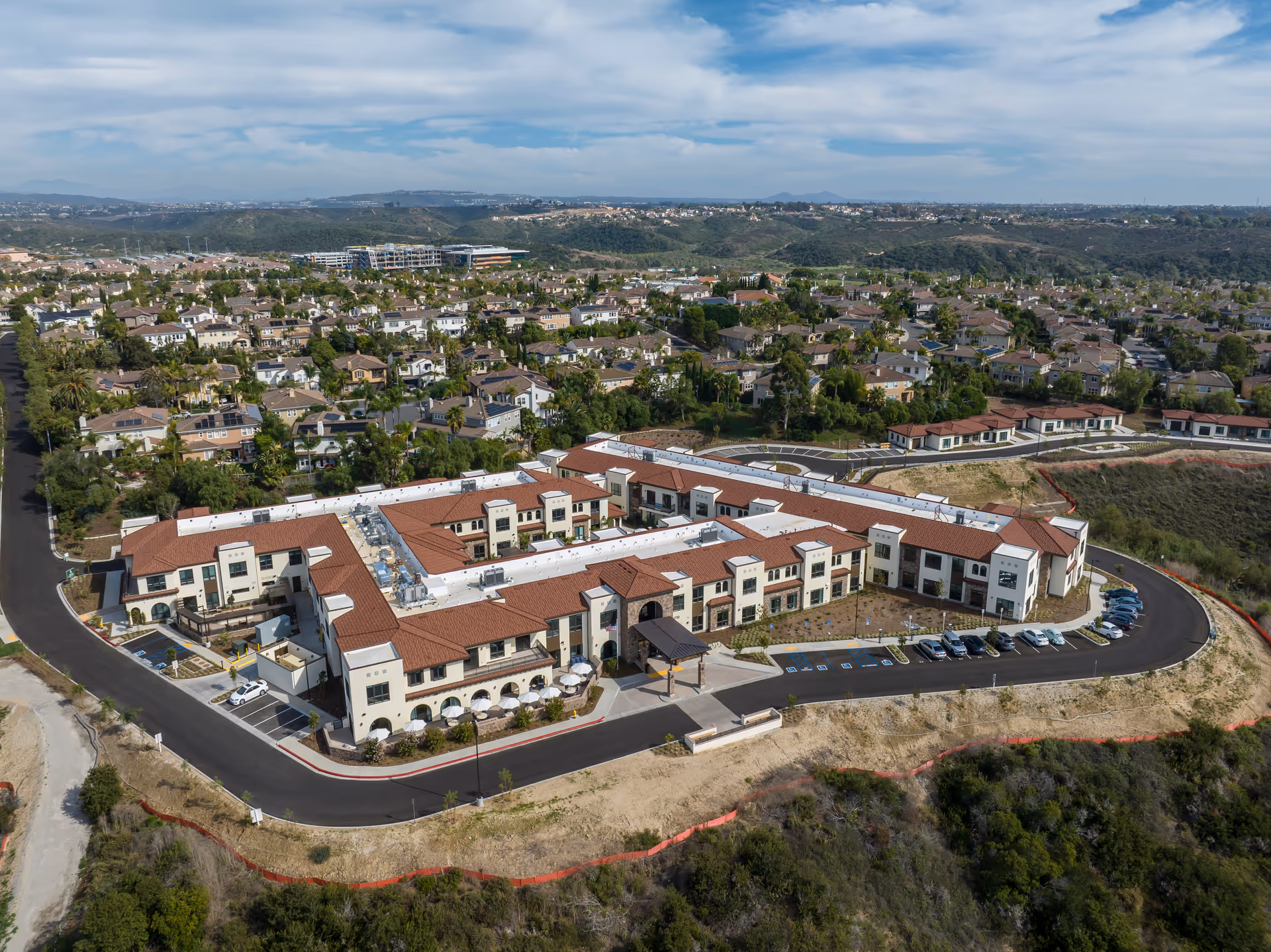 Aerial view of the Westmont of Carmel Valley senior living complex with red-tiled roofs surrounded by homes and rolling hills.
