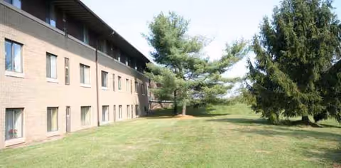 Two-story brick senior living building beside a well-kept grassy lawn and trees.