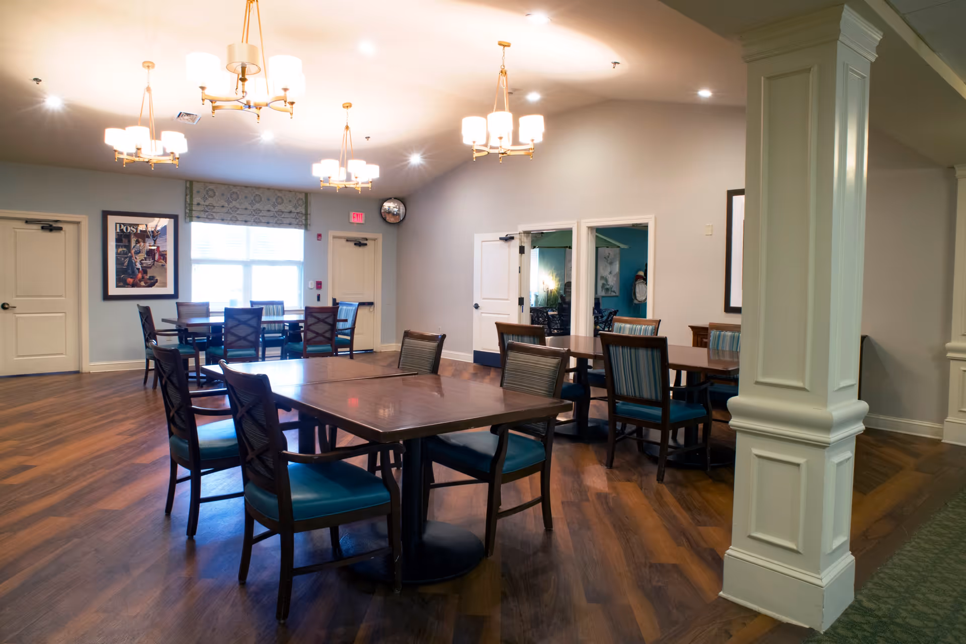 Open dining room with several wooden tables and teal-upholstered chairs under ceiling chandeliers.