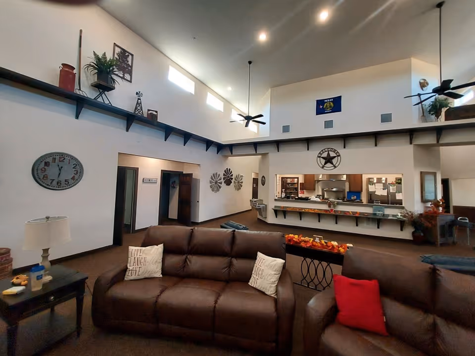 Spacious communal living room with leather sofas facing a serving counter under a high vaulted ceiling with ceiling fans.