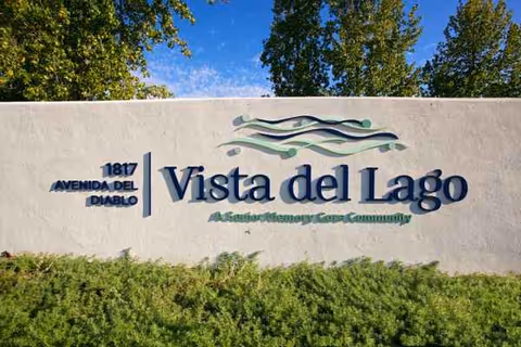 Exterior Vista del Lago Memory Care sign on a light wall with greenery.