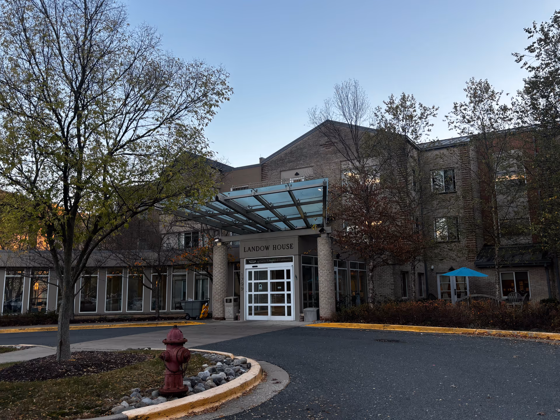 Front entrance of the three-story brick Landow House building with a glass canopy over the driveway.
