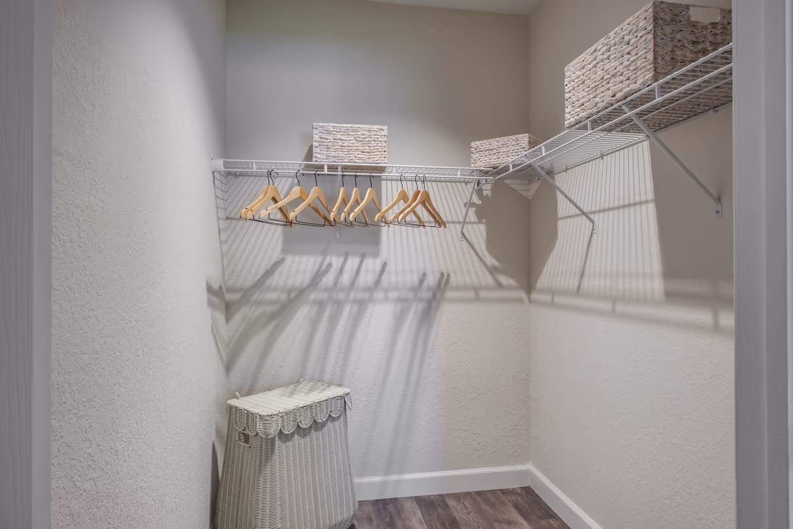 Empty walk-in closet with wire shelving, wooden hangers, woven storage baskets, and a laundry hamper on wood-look flooring.