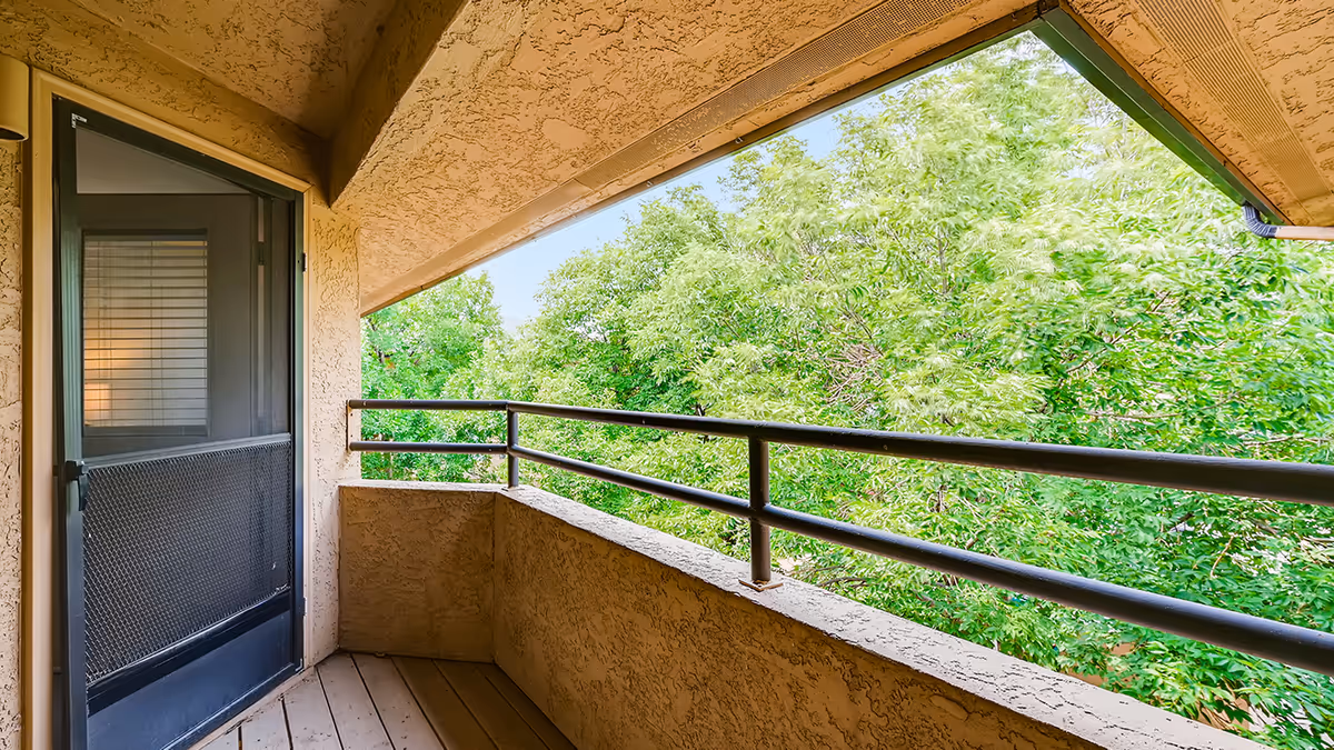 Covered stucco balcony with a metal railing overlooking leafy green trees.
