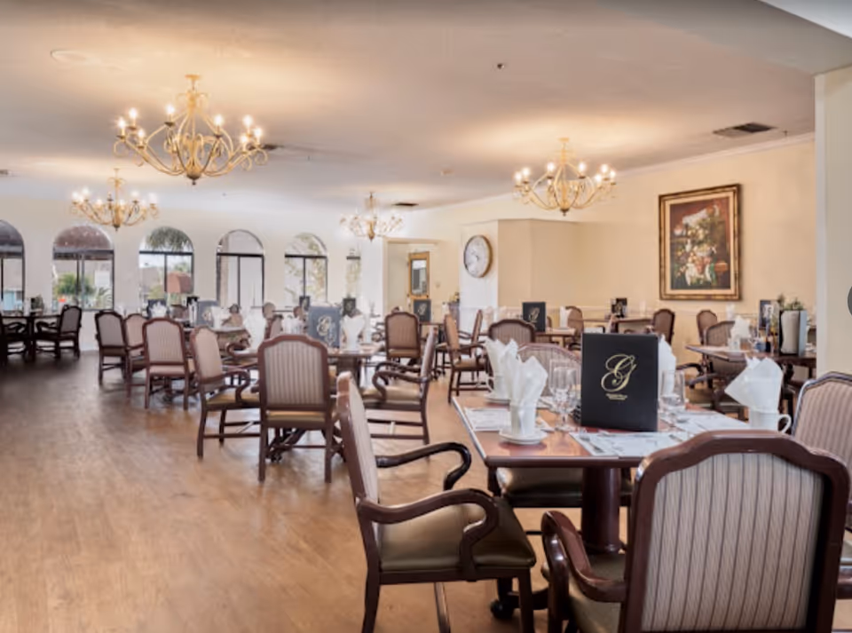 Spacious dining room with multiple set tables and upholstered chairs, chandeliers, and large arched windows.