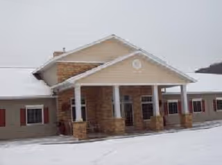 Snow-covered senior living facility exterior with a covered entrance and brick columns.