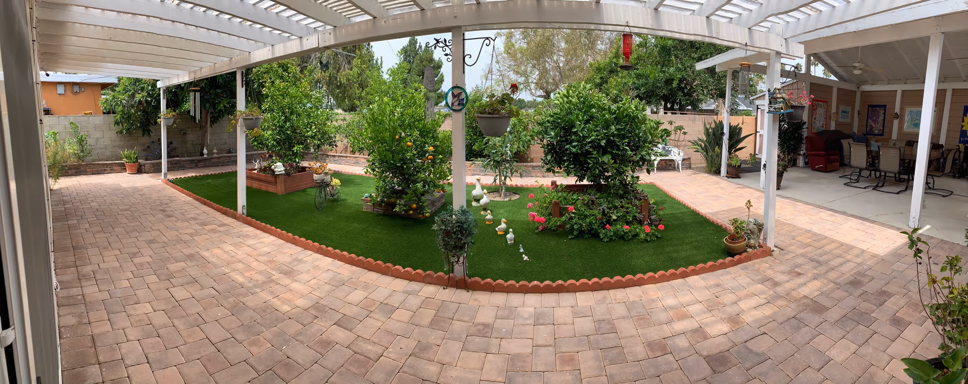 Outdoor courtyard with brick paving, garden beds, potted plants, and a covered seating area.
