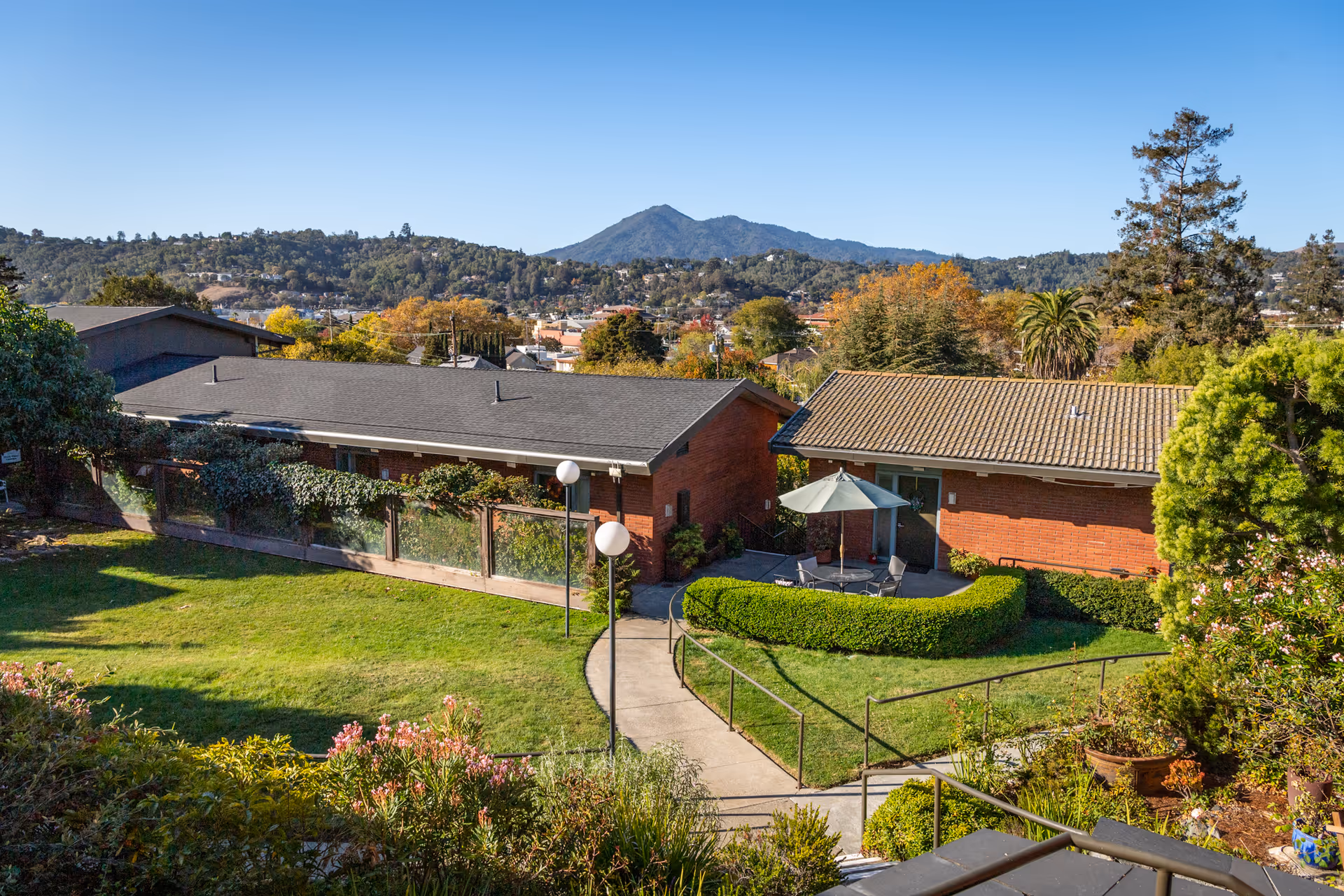 Courtyard with walkways, green lawn, patio seating and two single-story brick buildings with hills and a mountain in the background.