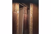 A shower area with a brown patterned shower curtain partially drawn, surrounded by tiled walls with a mosaic tile border.