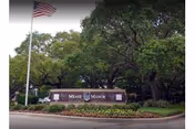 Brick entrance sign reading "Mease Manor" set in landscaped grounds with trees and an American flag on a pole.