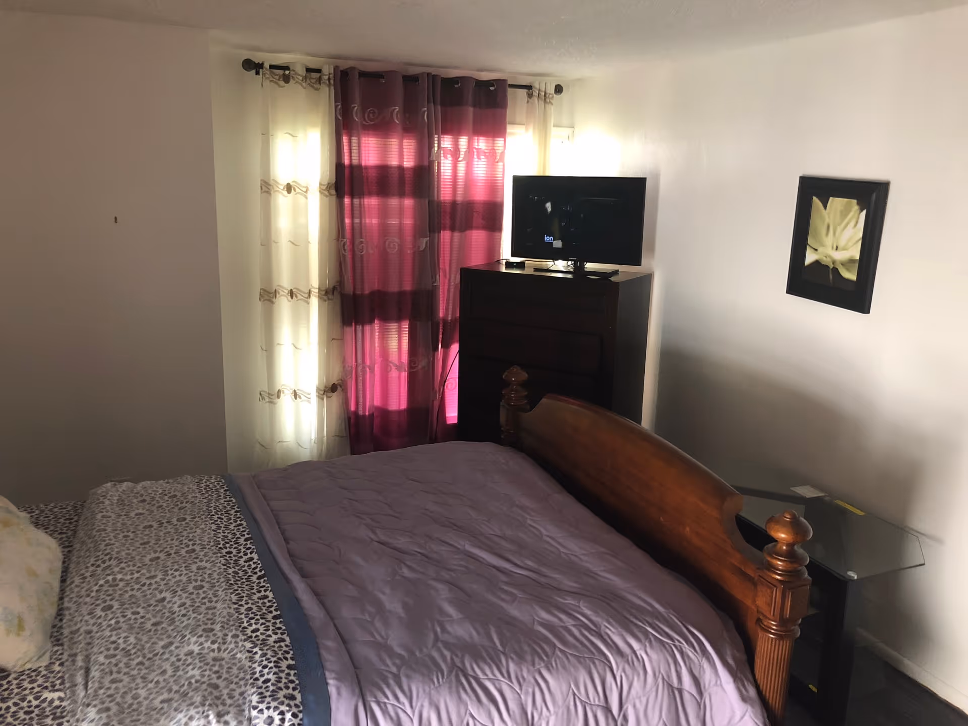 Bedroom in a senior living facility featuring a bed, dresser, TV, and purple curtains.