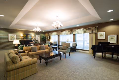 Spacious, well-lit lounge with sofas, armchairs, a coffee table, grand piano, and large windows with drapes.