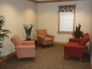 A cozy waiting lounge with chairs, plants, and a window in a senior living facility.