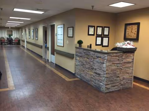 Long hallway inside a senior facility with a stone-front reception desk and framed certificates.