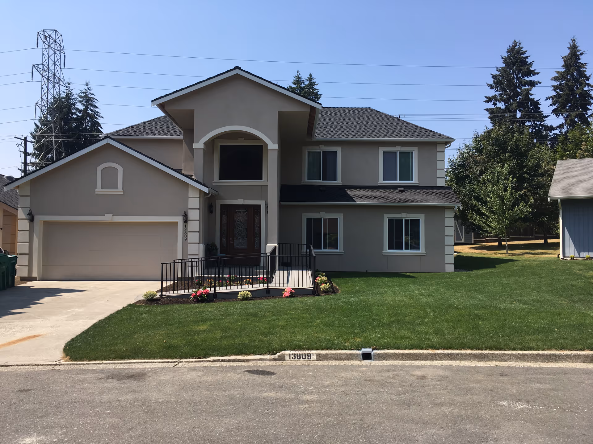 Two-story beige suburban house with an attached garage, front porch, railing and a neatly mowed lawn.