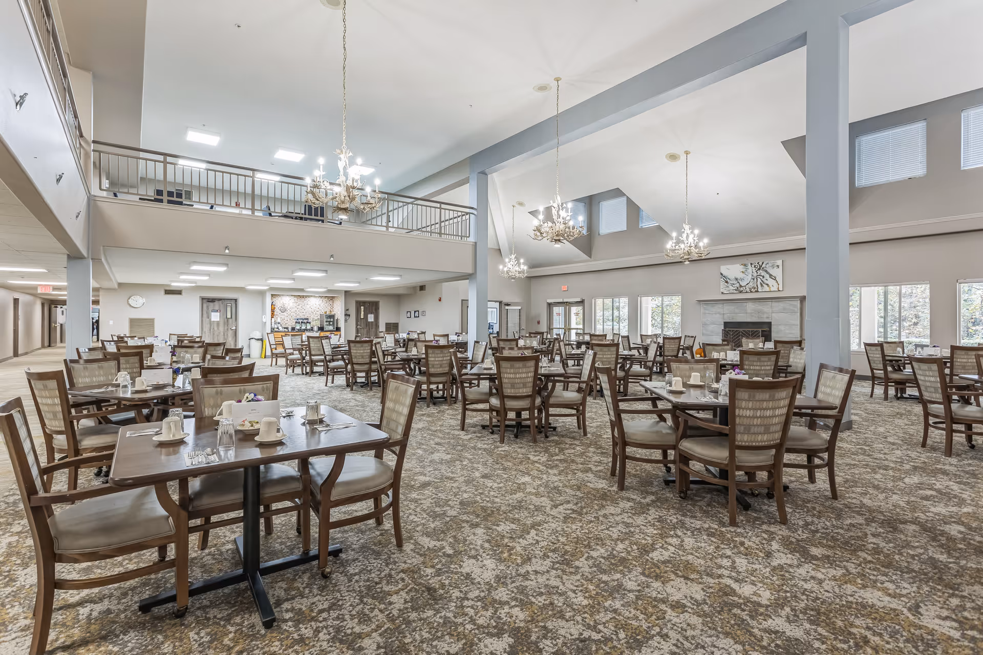 Large dining room with many set tables and chairs, chandeliers, a high vaulted ceiling and a fireplace.