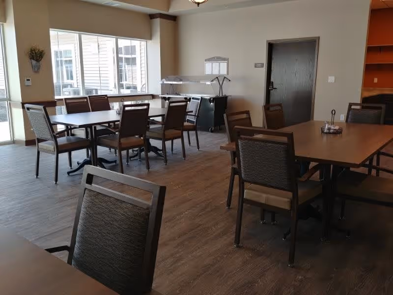 Spacious dining room with multiple wooden tables and chairs, large windows, and a serving station.